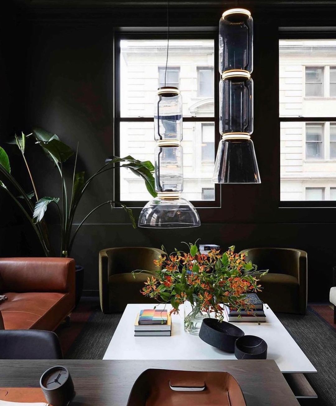 Stacked glass cylinders and a dome from Clérachic hang in a dark lounge with a leather sofa and a flower arrangement.