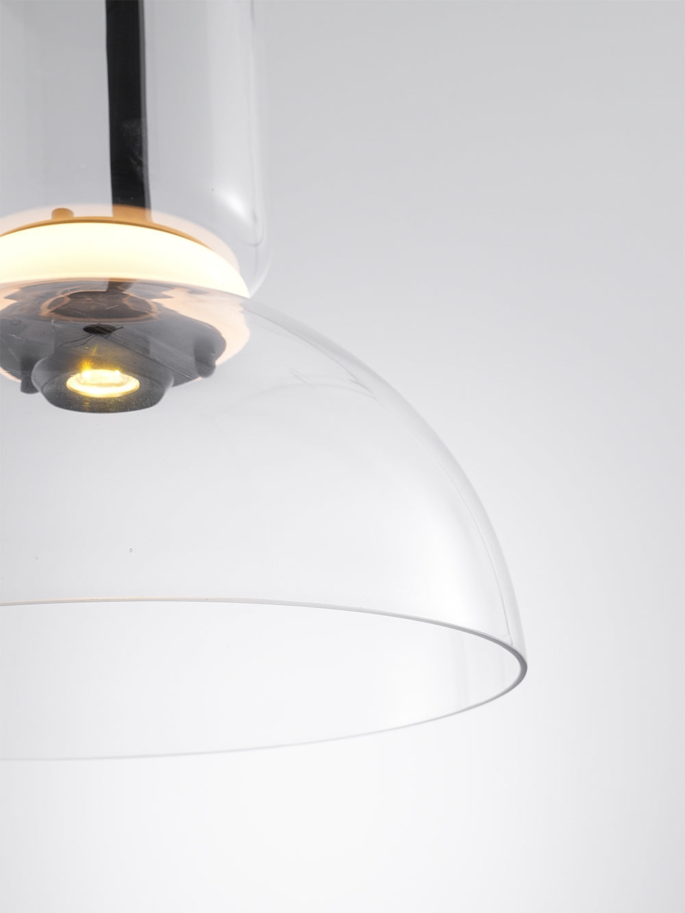 Close view of the glowing ring, the small light source and the edge of the clear glass dome on this Clérachic pendant.