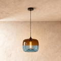 Clérachic glass pendant in amber fading to blue, lit by a warm filament bulb, hung on a black cord from a black canopy.