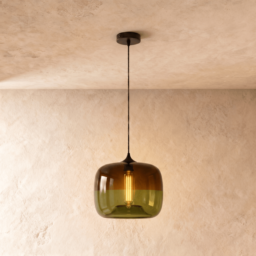 Clérachic glass pendant in amber fading to olive green, lit by a warm filament bulb, hung on a black cord from a black canopy.