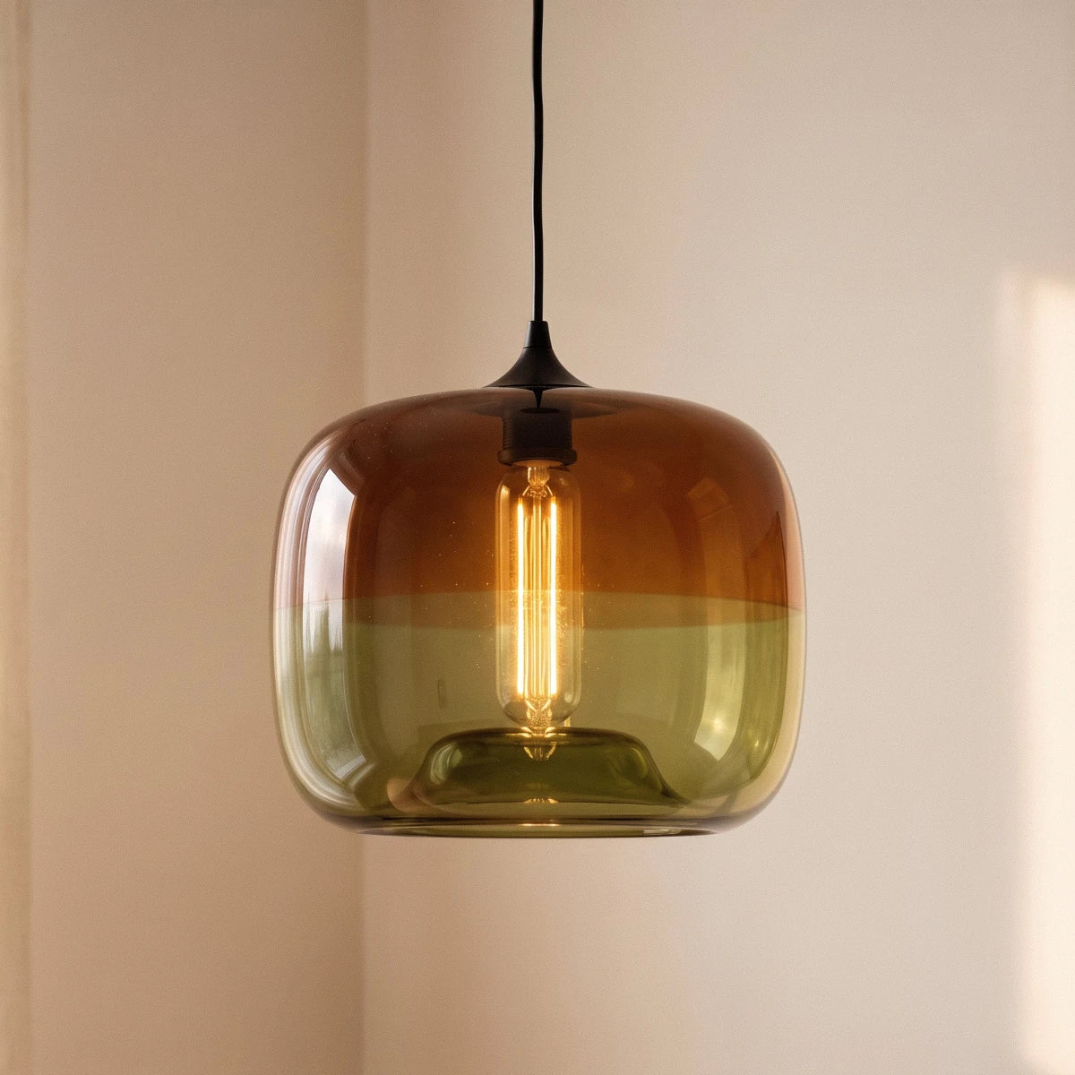 Clérachic amber-to-green glass pendant shown close, its rounded shade enclosing a warm filament bulb on a black cord.