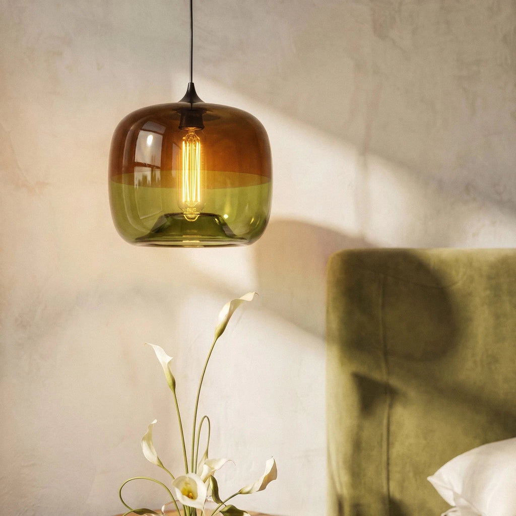 Close-up of the Clérachic amber-to-olive glass pendant, its warm filament bulb lighting the shade above white calla lilies.