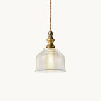Pendant light from Clérachic with a ribbed clear glass dome, an antique brass fitting and a twisted fabric cord, on a plain white backdrop.