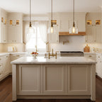 Three Clérachic ribbed glass pendants hang in a row above a marble-topped kitchen island with cream cabinets and brass taps.