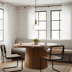 A single Clérachic clear glass pendant hangs over a round wooden table in a breakfast nook, with black-framed windows behind.