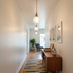 Looking down a hallway, a Clérachic glass pendant hangs in the foreground with more in a line beyond, above a wooden sideboard.