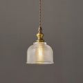 Close view of a Clérachic pendant's ribbed glass dome and turned antique brass fitting, with a twisted cord, against a grey wall.