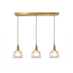 Three-light linear Clérachic pendant with ribbed glass domes on twisted cords, hung from a long brass canopy bar, on white.
