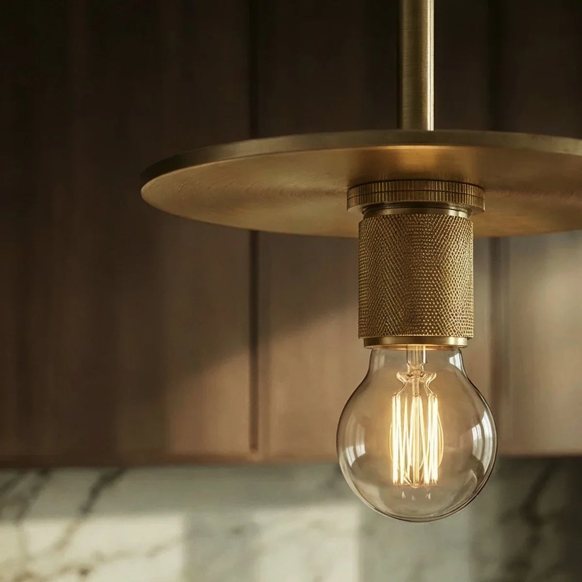 Clérachic brass pendant light in close detail, showing the flat disc shade and knurled socket above an exposed bulb.