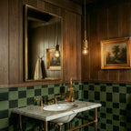Clérachic brass pendant lights with exposed bulbs glowing above a marble vanity in a dark green-tiled bathroom.