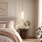 A single Clérachic frosted glass pendant on a thin brass rod hangs beside a bed with blush bedding and a round fluted wooden side table.