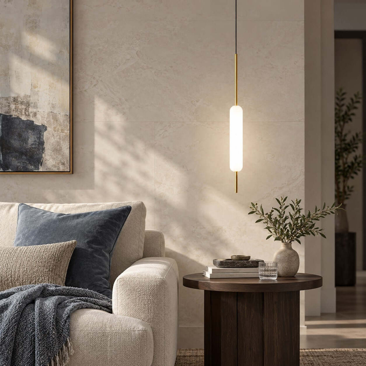 This Clérachic single brass and frosted glass pendant glows above a round dark side table, beside a boucle sofa with navy cushions.