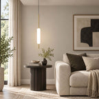 Hanging over a dark round side table and a cream armchair, this Clérachic frosted glass pendant on a brass rod is lit against a neutral wall.