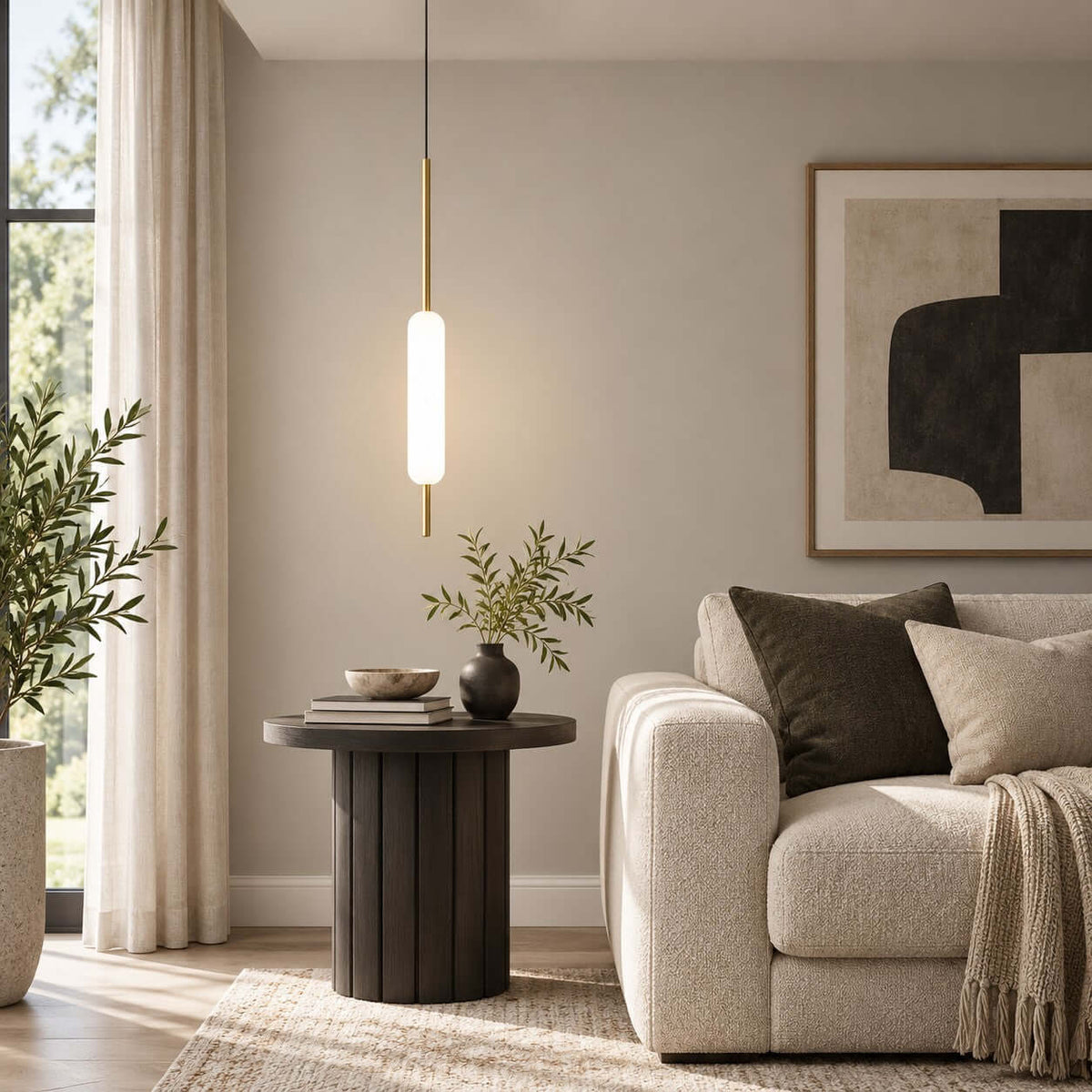 Hanging over a dark round side table and a cream armchair, this Clérachic frosted glass pendant on a brass rod is lit against a neutral wall.