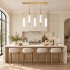 Five lit Clérachic glass pendants on brass rods hang above a marble kitchen island with four pale counter stools and a marble splashback.