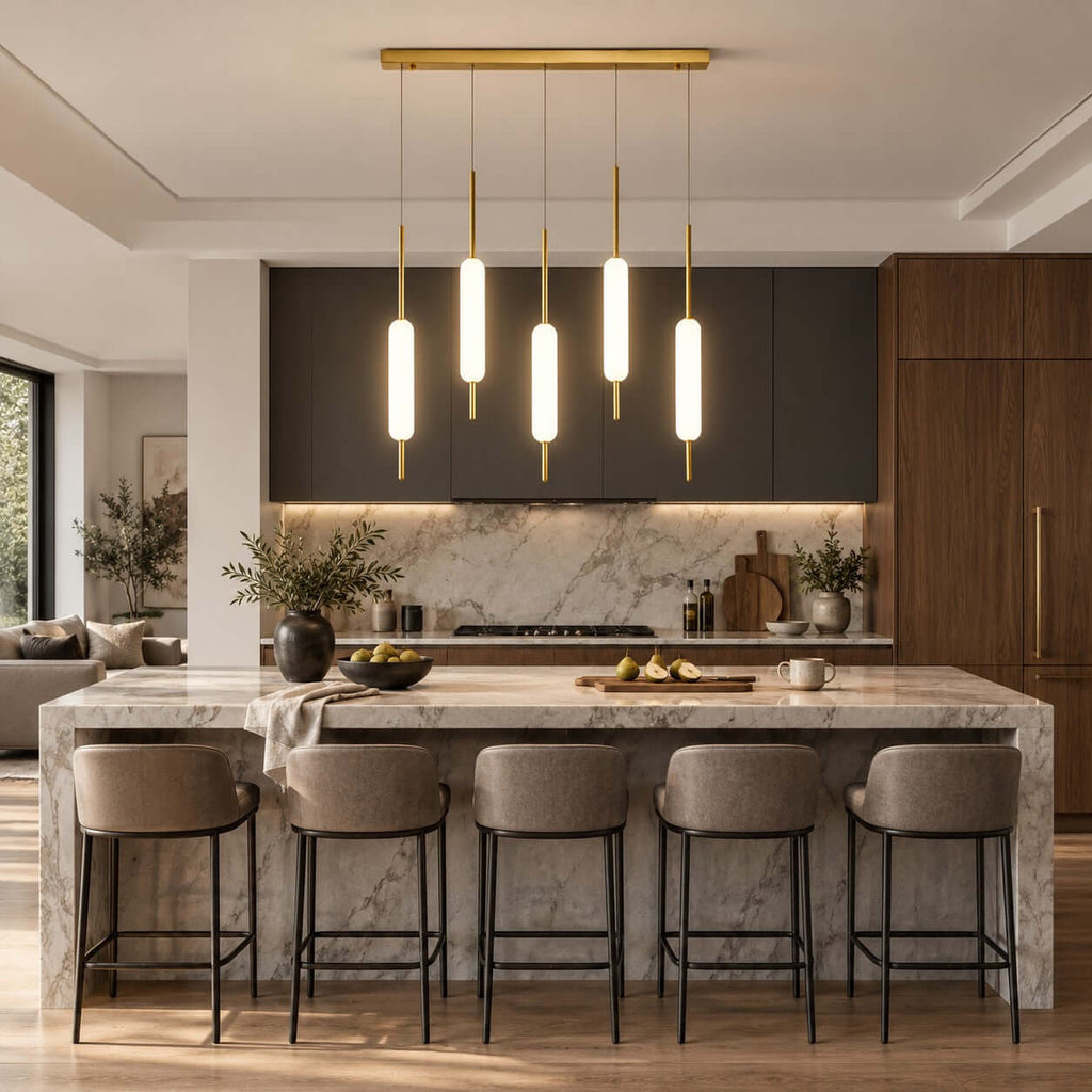 Five Clérachic pendants on a long brass bar hang in a dark-cabinet kitchen with a marble island and five grey leather stools.