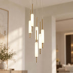 Close view of a lit Clérachic pendant cluster at different heights, frosted glass cylinders on thin brass rods against a cream wall.