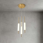 Three lit Clérachic frosted glass pendants on brass rods hang from a round brass canopy against a grey plaster wall.