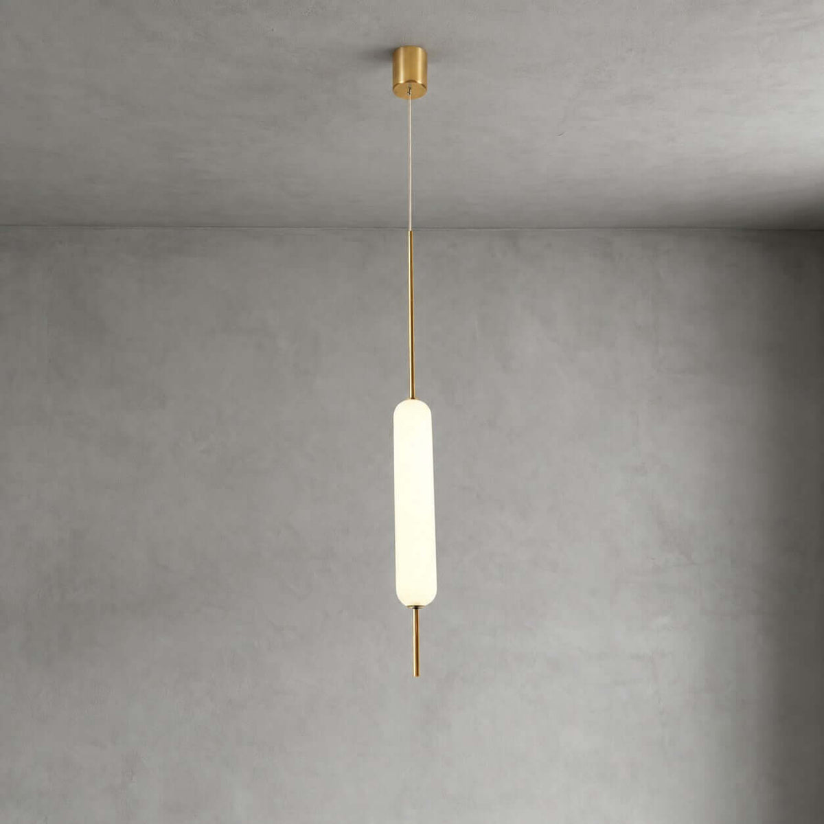 One lit Clérachic frosted glass pendant on a thin brass rod hangs from a small brass canopy against grey plaster.