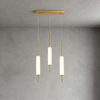 Three Clérachic frosted glass pendants at different heights hang from a slim brass bar against a grey plaster wall.