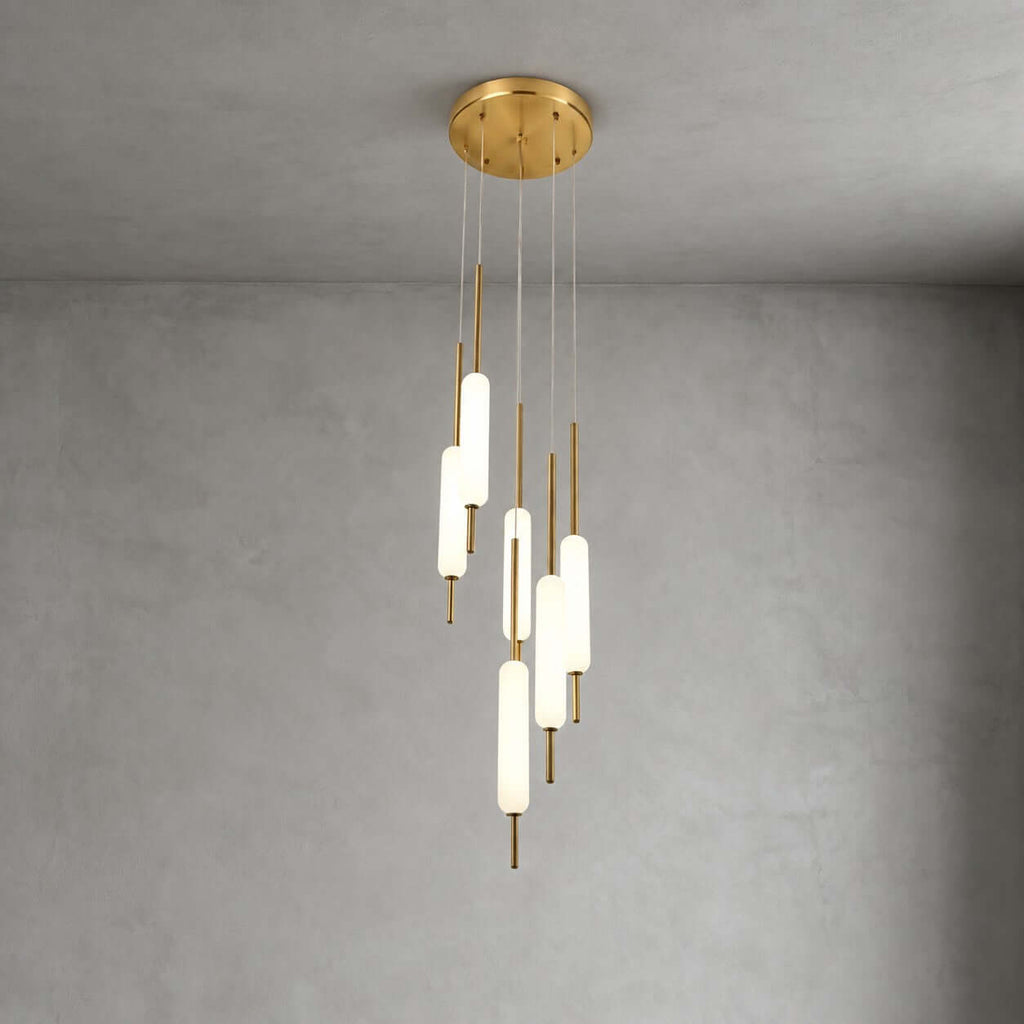 A cluster of Clérachic frosted glass pendants hangs from a round brass canopy against grey plaster, in a larger layout than the three-light.