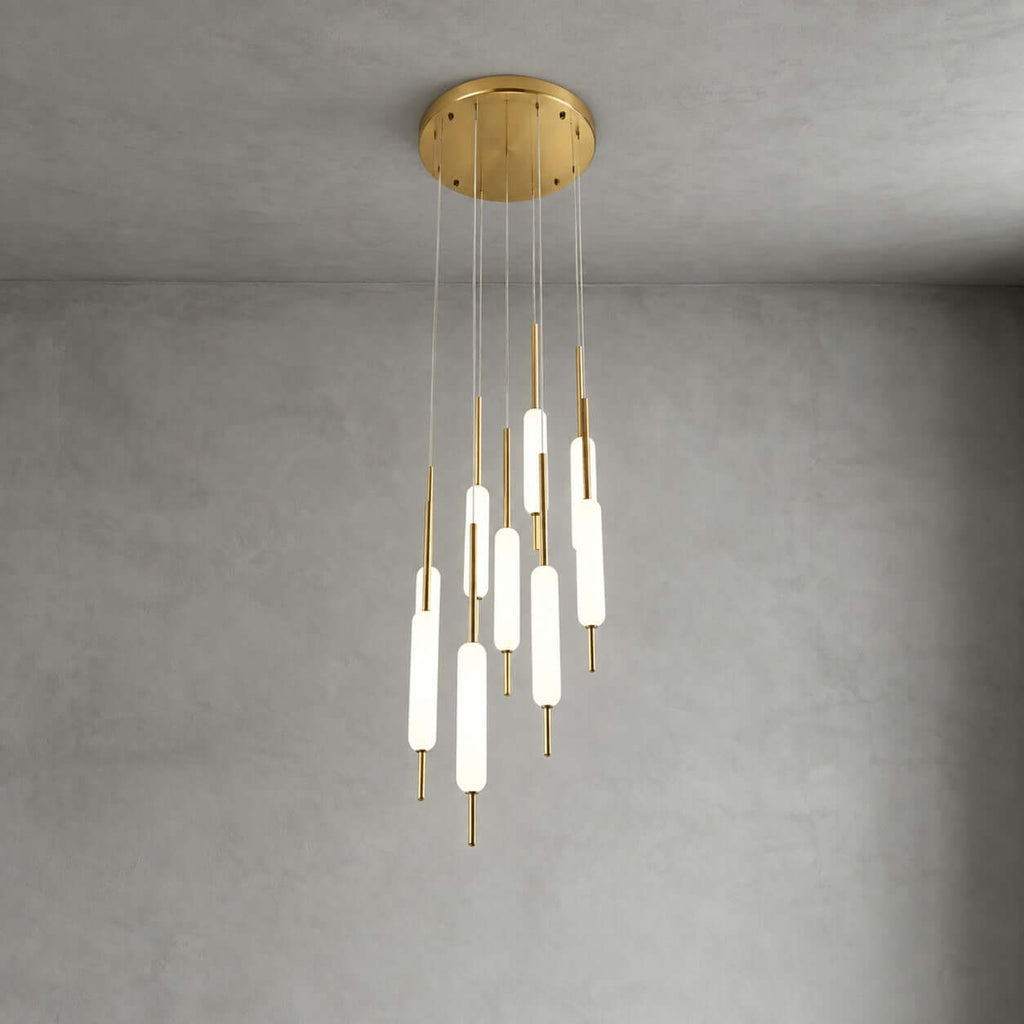 A large cluster of lit Clérachic frosted glass pendants on brass rods hangs from a round brass canopy in front of a grey wall.