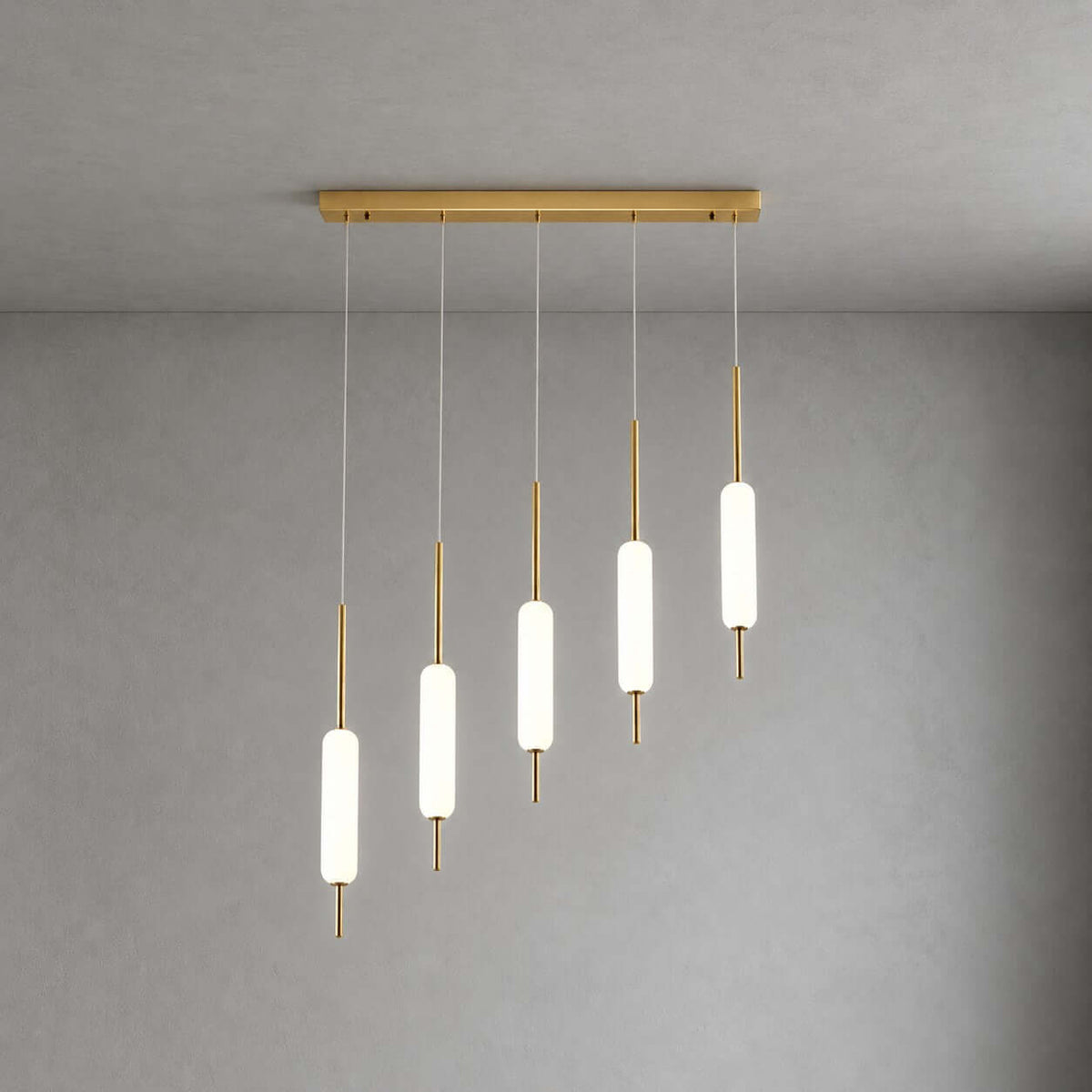 Five Clérachic frosted glass pendants step down in height from a long brass bar, lit against a grey plaster wall.