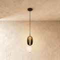 Clérachic stacked glass pendant, smoked amber capsule above an opal globe, glowing on a slim black cord against limewash.