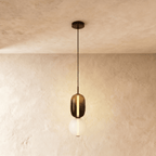Clérachic stacked glass pendant, smoked amber capsule above an opal globe, glowing on a slim black cord against limewash.
