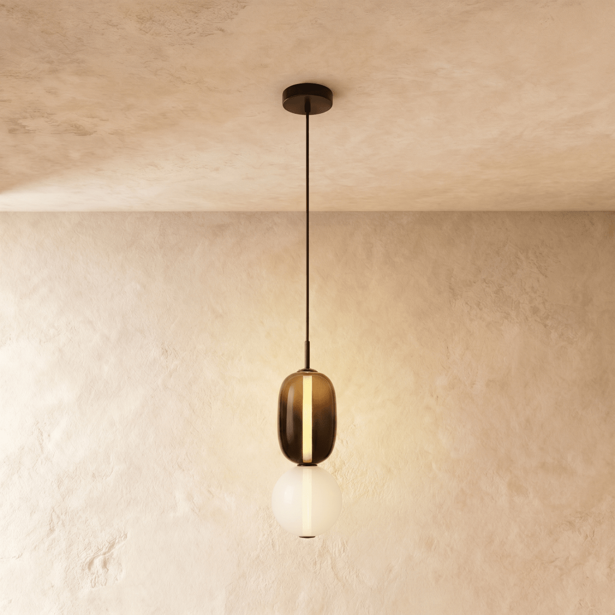 Clérachic stacked glass pendant, smoked amber capsule above an opal globe, glowing on a slim black cord against limewash.