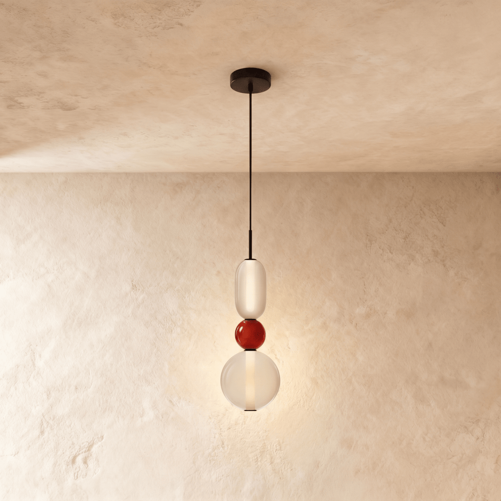 Clérachic pendant stacking a frosted capsule, a small red glass bead and a clear globe, lit softly on a black cord.