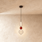 Clérachic pendant stacking a frosted capsule, a small red glass bead and a clear globe, lit softly on a black cord.