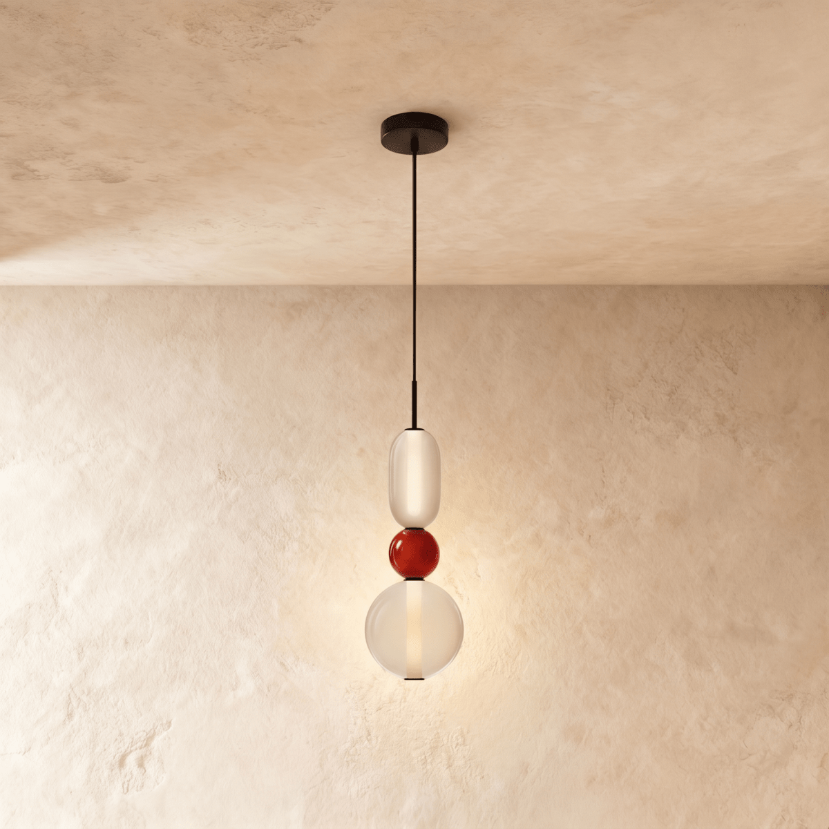 Clérachic pendant stacking a frosted capsule, a small red glass bead and a clear globe, lit softly on a black cord.