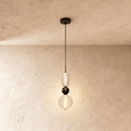 Clérachic pendant in frosted white glass with a black glass bead between the capsule and globe, glowing on a limewash wall.