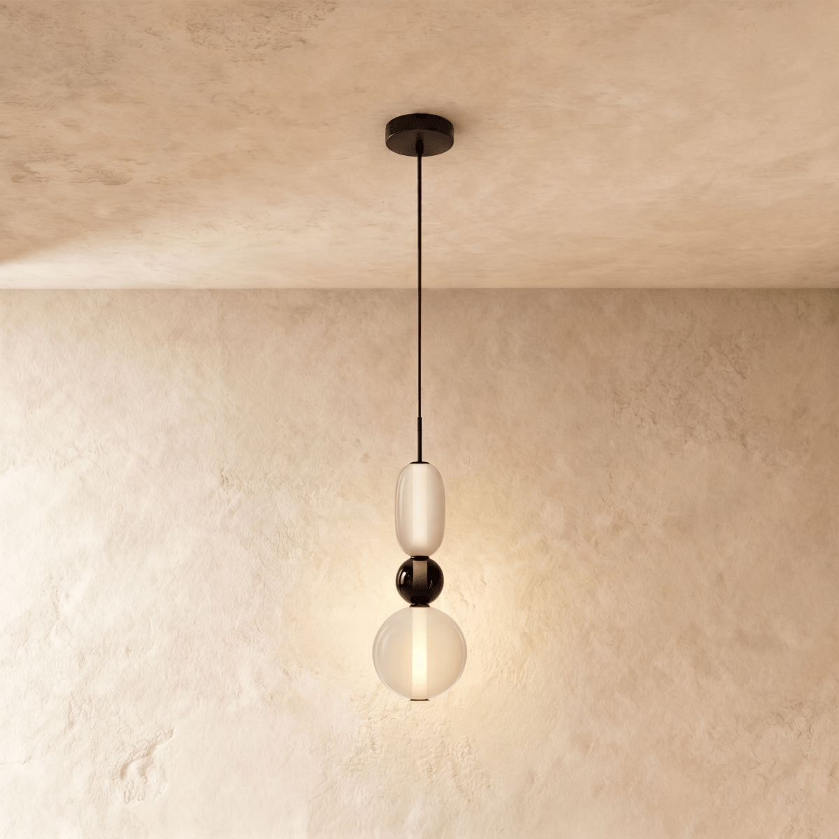 Clérachic pendant in frosted white glass with a black glass bead between the capsule and globe, glowing on a limewash wall.