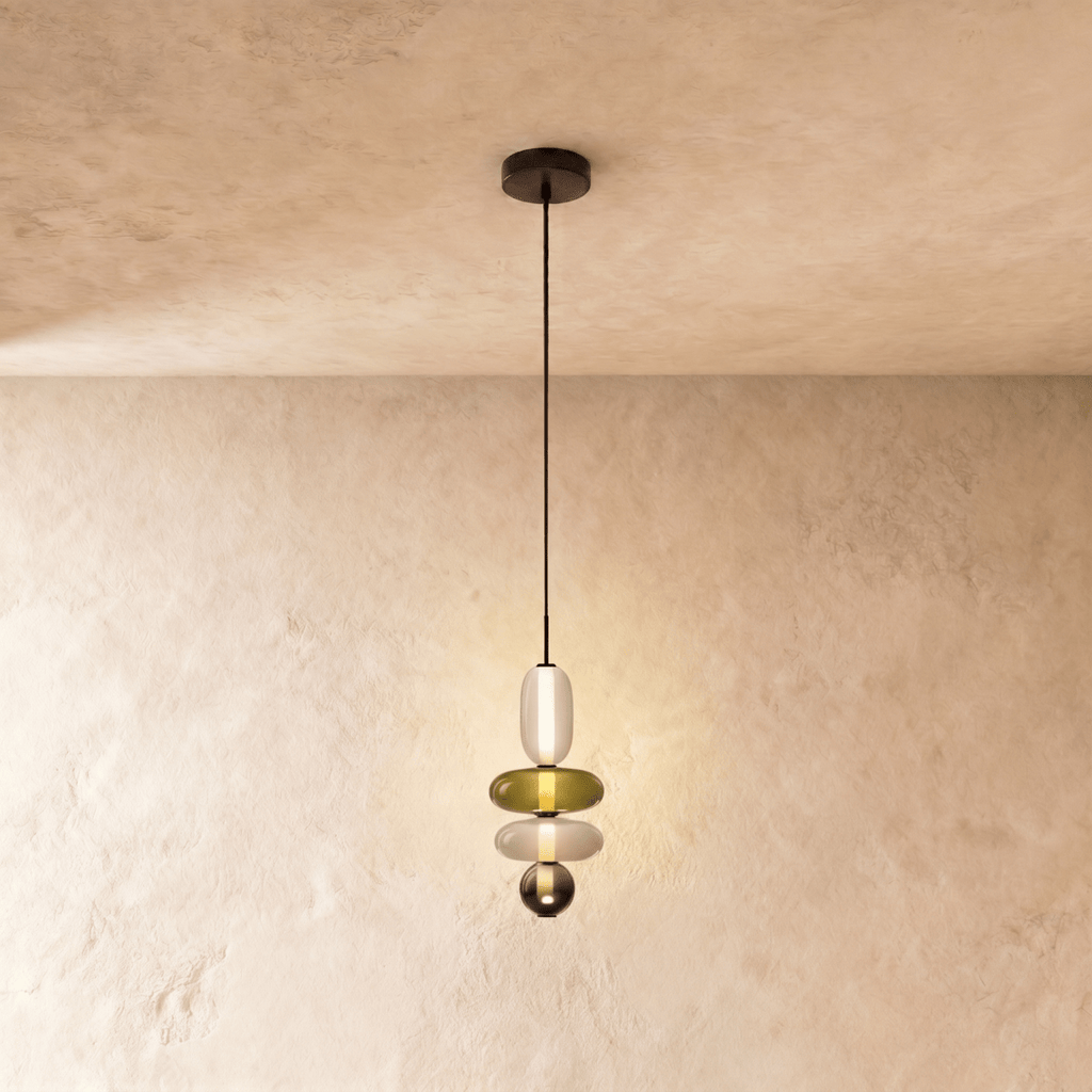 Clérachic slim pendant of a frosted capsule, olive disc, white disc and a small smoked glass bead, softly lit.