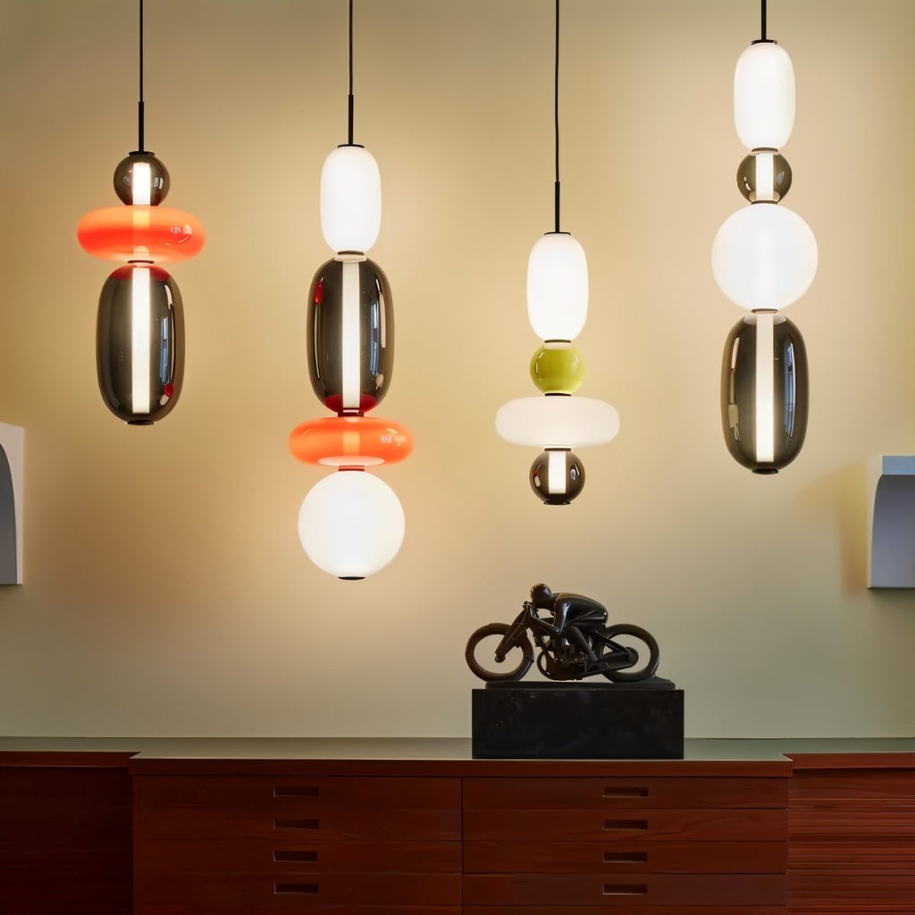 Clérachic stacked glass pendants in four colour mixes hung side by side above a walnut sideboard with a bronze sculpture.