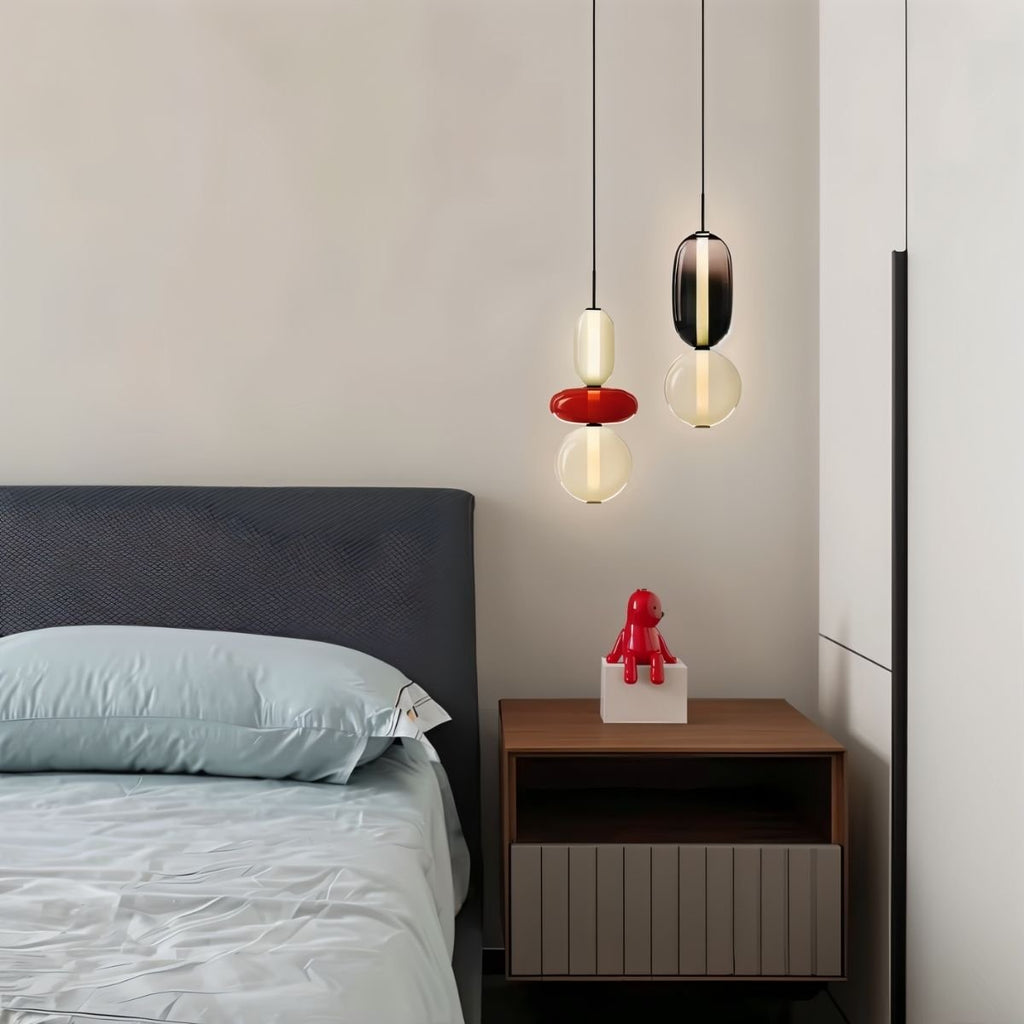 Clérachic pair of glass pendants beside a bed, one with a red disc and one smoked, used as bedside lighting.