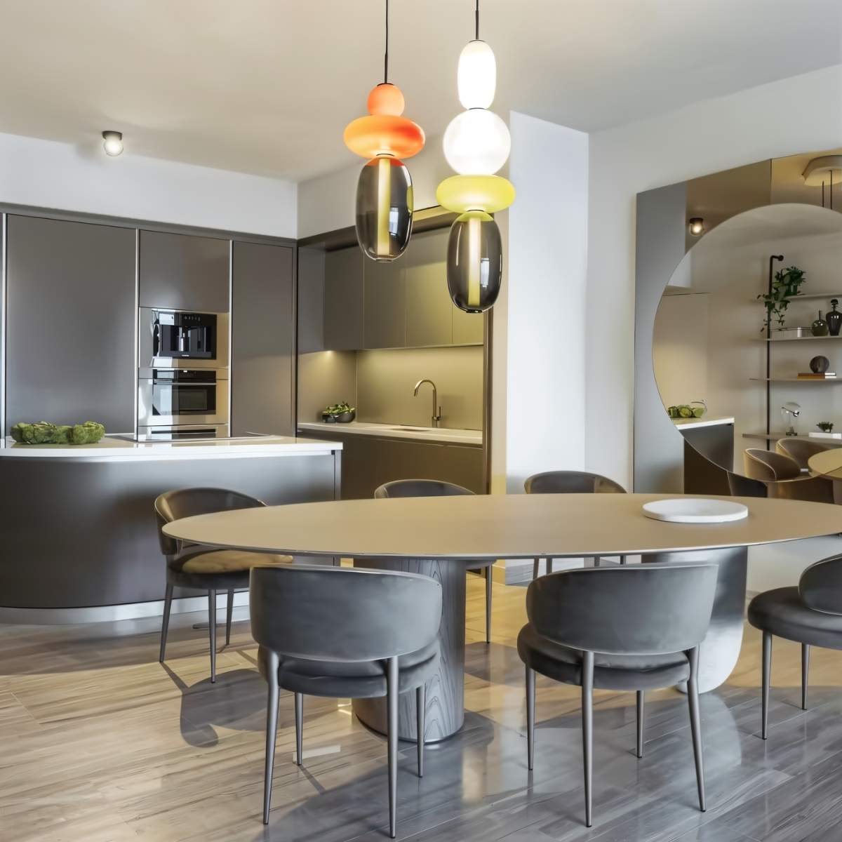 Clérachic stacked glass pendants in orange, yellow and smoked tones above a long oval dining table and open kitchen.