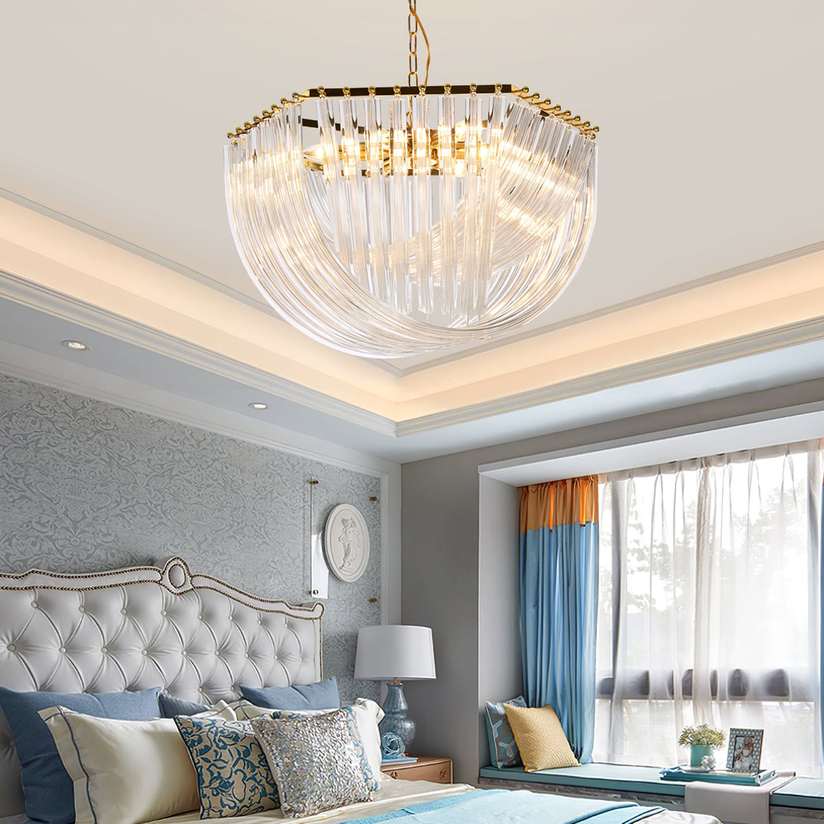 Clérachic chandelier lit above a bedroom with a grey tufted headboard, blue and orange curtains and a ceiling cove light.