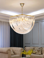 Clérachic chandelier on a gold chain above a cream tufted sofa, with grey curtains and yellow flowers in the foreground.