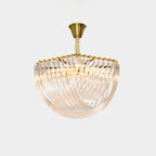 Clérachic chandelier with a brass canopy, a looped clear glass rod bowl and a warm glow from within, on a pale grey backdrop.