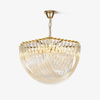 Gold-framed glass chandelier with curved clear glass rods sweeping into a bowl shape, hung from a gold chain on a plain white backdrop from Clérachic.