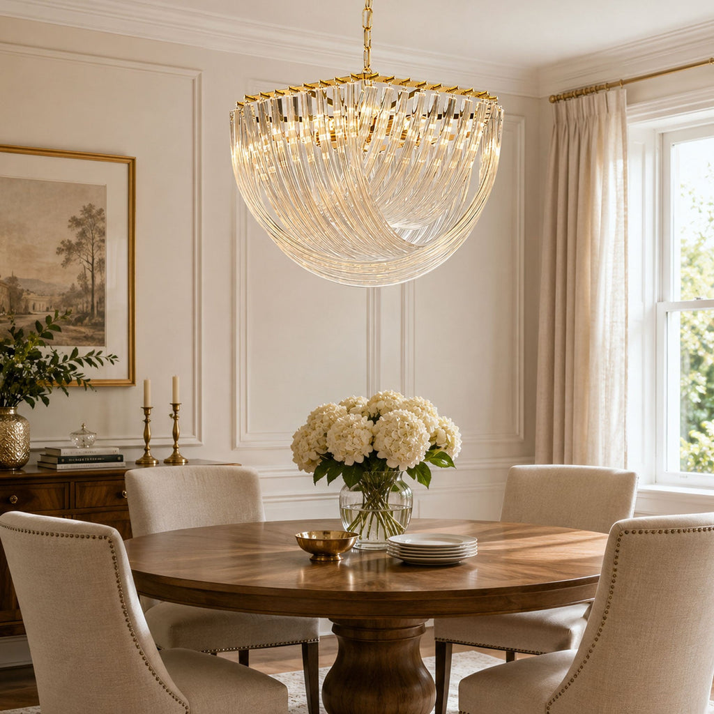 Lit Clérachic glass rod chandelier above a round wooden dining table in a cream room with hydrangeas and a framed landscape.