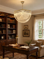 Warm-lit Clérachic chandelier hanging in a study with a dark wood desk, a bookcase full of books and a leather armchair.