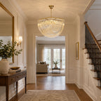 Clérachic chandelier lit in a panelled hallway with a wooden console table, a staircase and a view through to the next room.