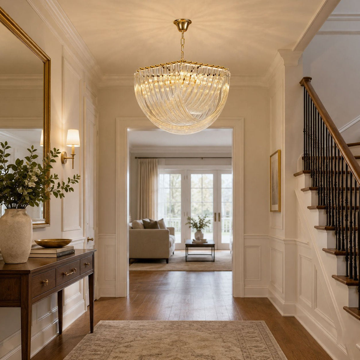Clérachic chandelier lit in a panelled hallway with a wooden console table, a staircase and a view through to the next room.