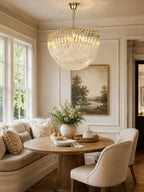 Clérachic glass chandelier in a bright breakfast nook with a round wooden table, cushioned seat and a landscape painting.
