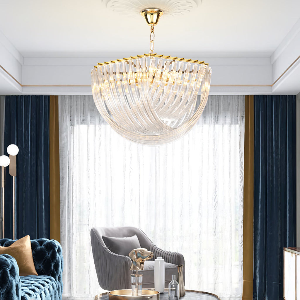 Large Clérachic glass chandelier in front of navy velvet curtains and a sheer window, above a blue tufted sofa and grey armchair.