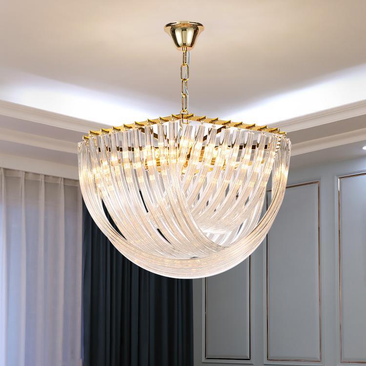 Close view from below of the curved clear glass rods and gold chain of this Clérachic chandelier, with grey panelling and curtains behind.